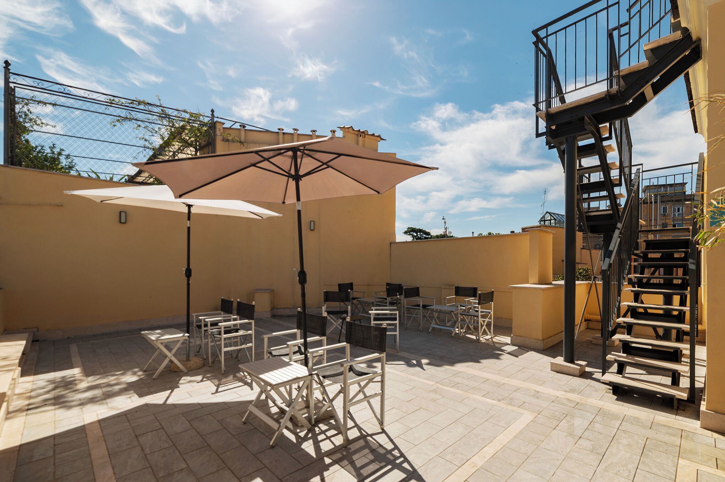 An outdoor patio area with tables and chairs, a large umbrella, and a staircase.