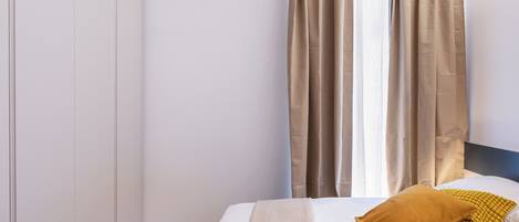 Una habitación de hotel con cama, cabecero y cortinas.