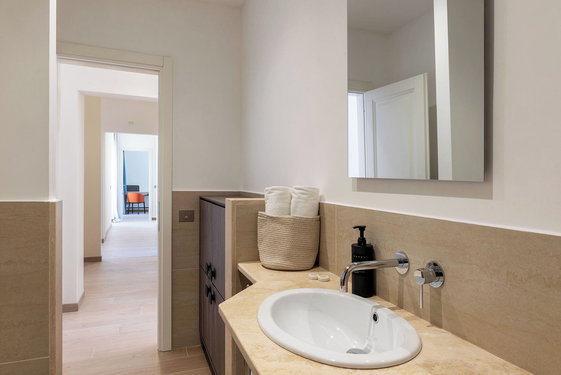 Een moderne badkamer met een grote wasbak, een spiegel en een mand voor handdoeken.