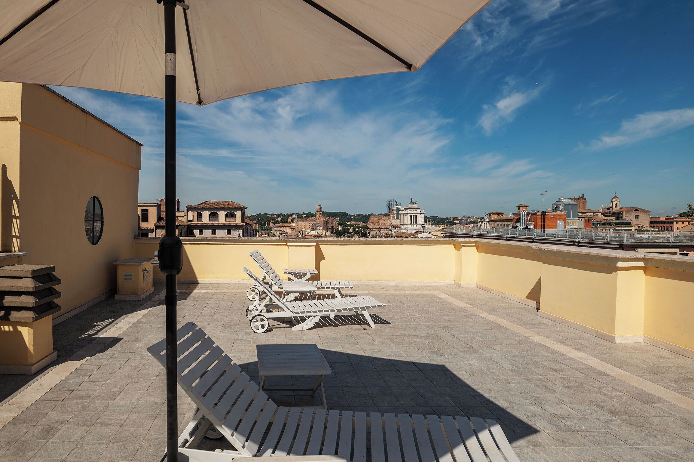 A rooftop terrace with lounge chairs, a table, and a large umbrella.