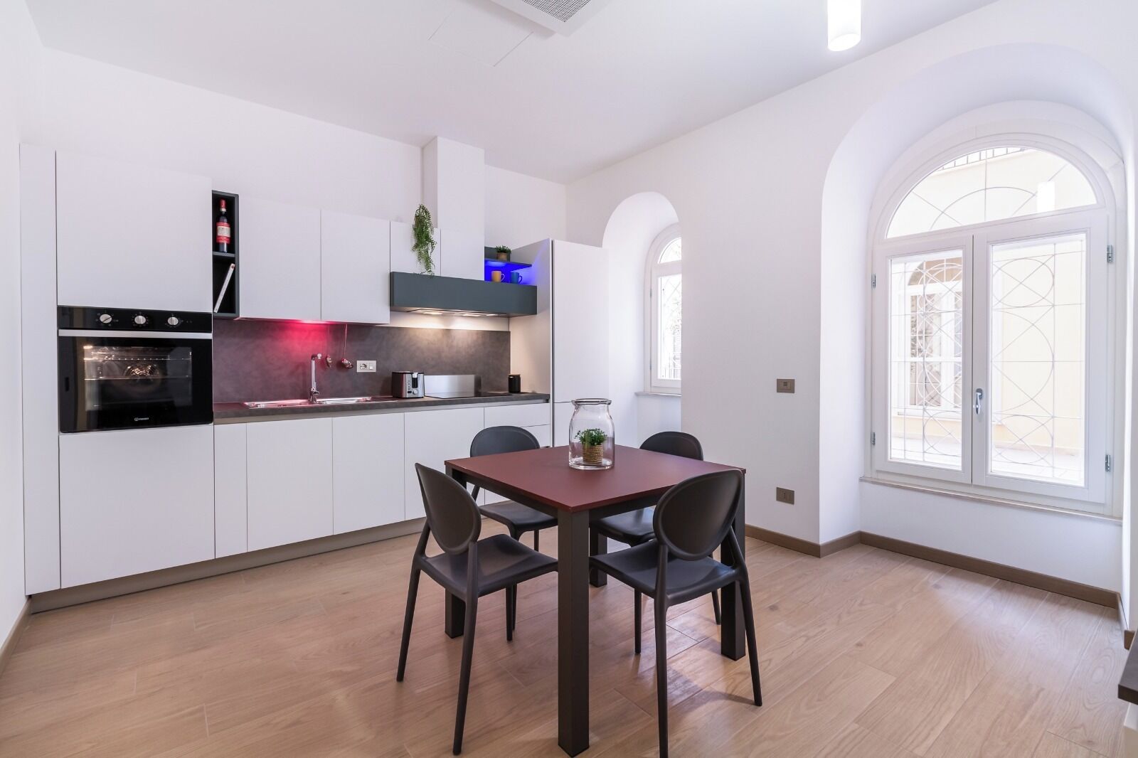 Una cocina moderna con armarios blancos, horno integrado y comedor con mesa y sillas de madera.