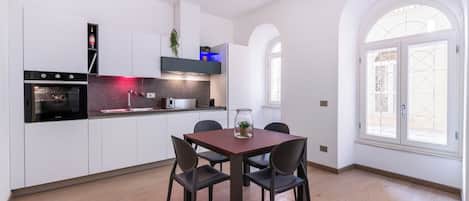A modern kitchen with white cabinetry, a built-in oven, and a dining area with a wooden table and chairs.