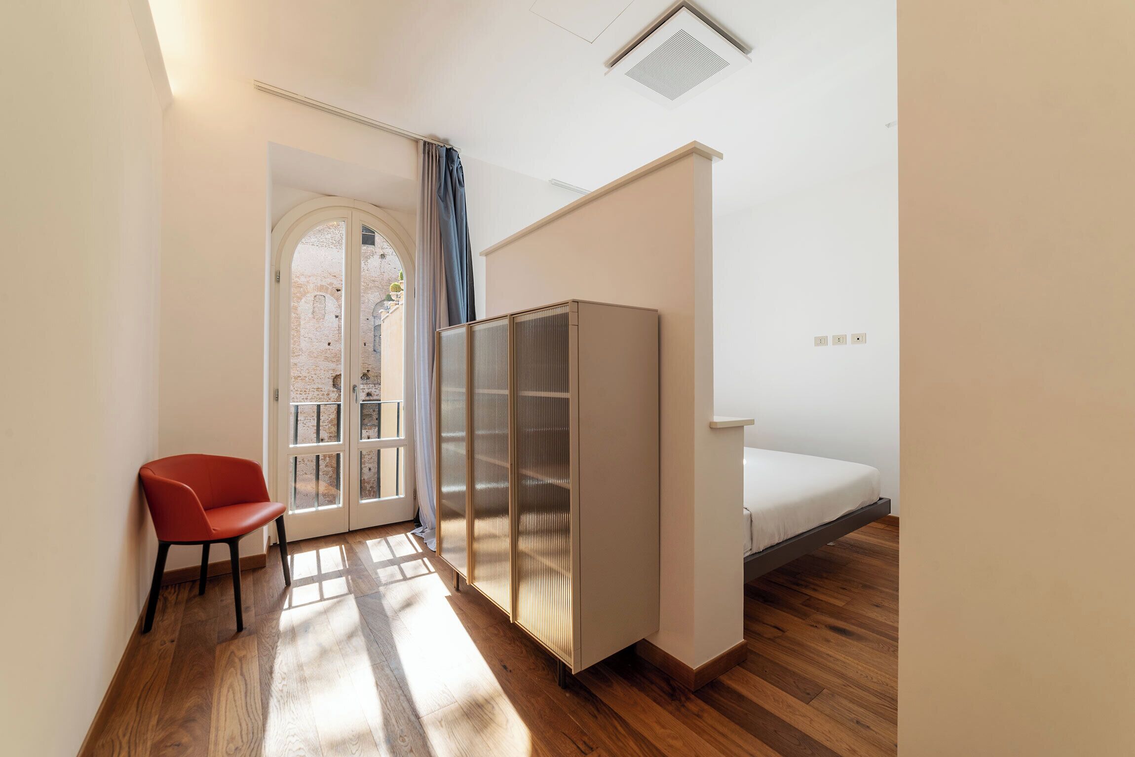 A compact room with a bed, a wardrobe, a chair, and a door leading to an outdoor area.