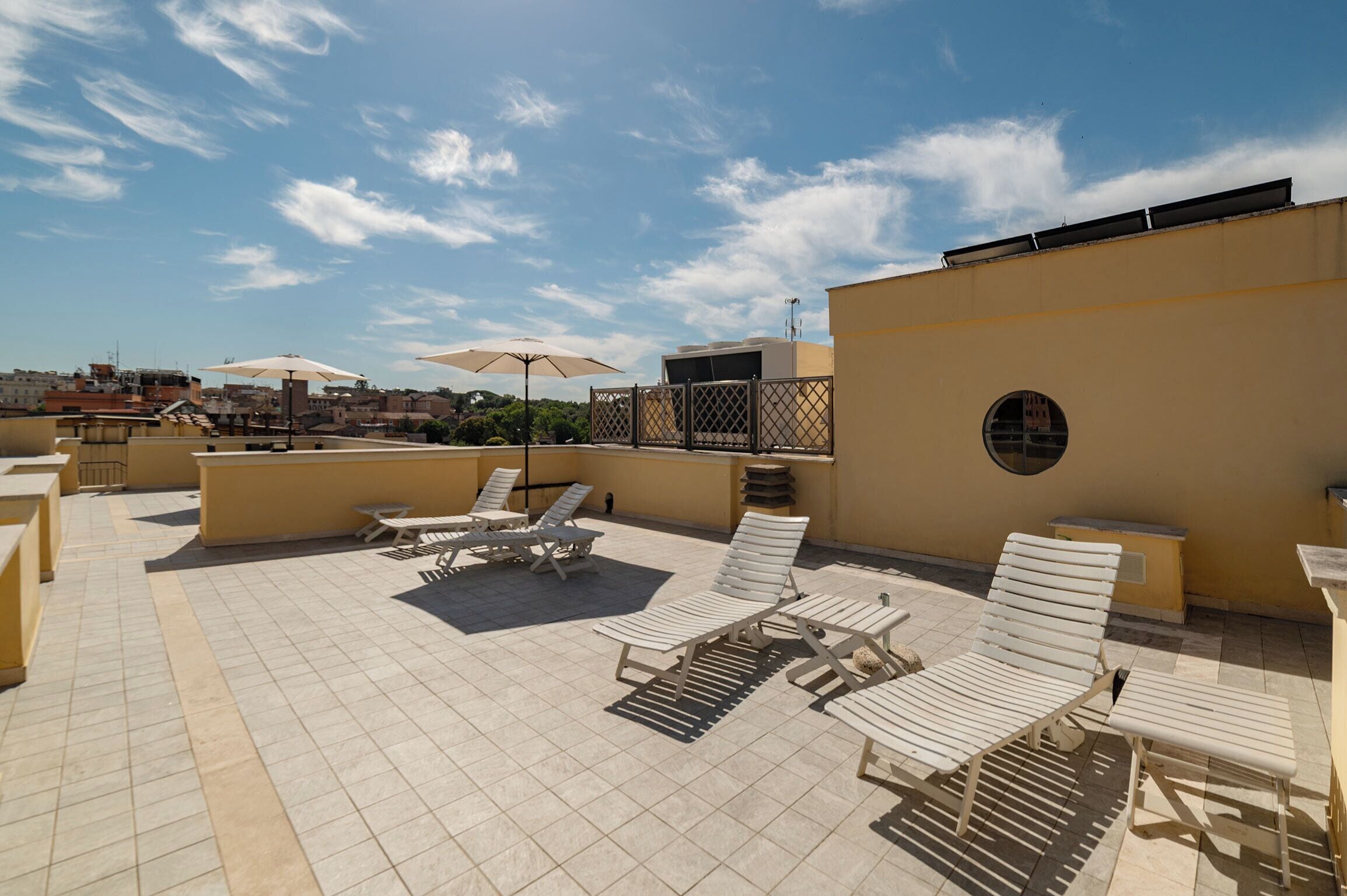A rooftop terrace with sun loungers, umbrellas, and a view of the cityscape.