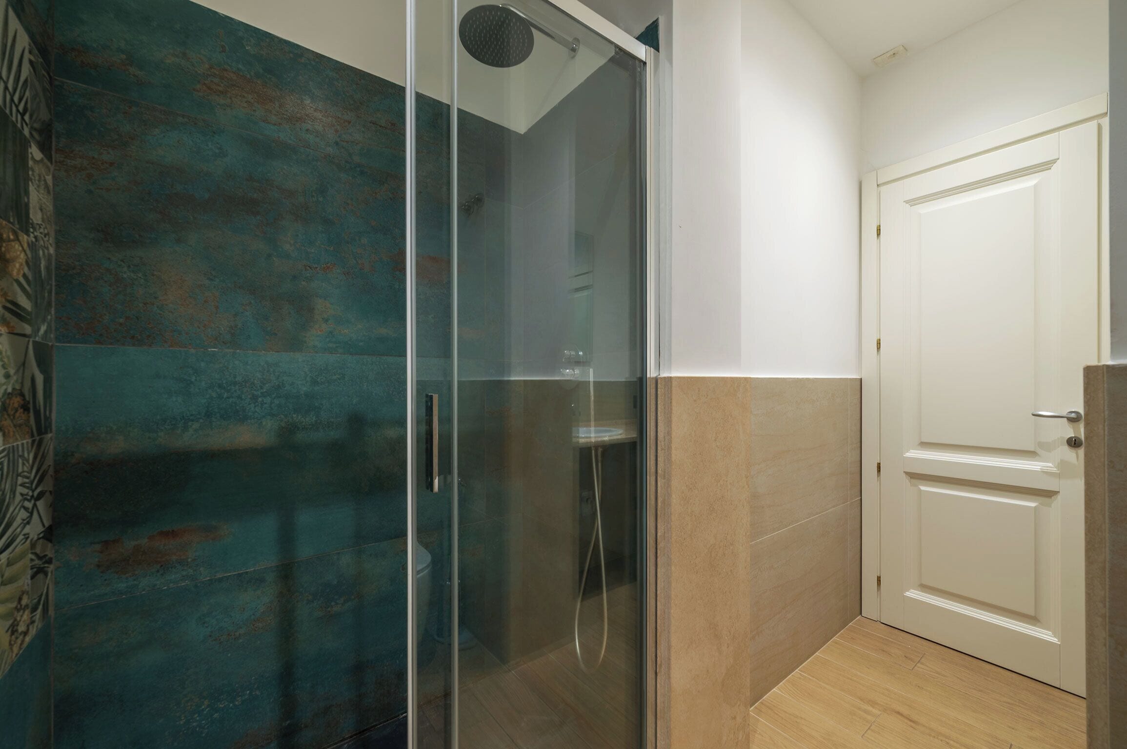 Ducha con cerramiento de vidrio, puerta blanca y pared de azulejos.