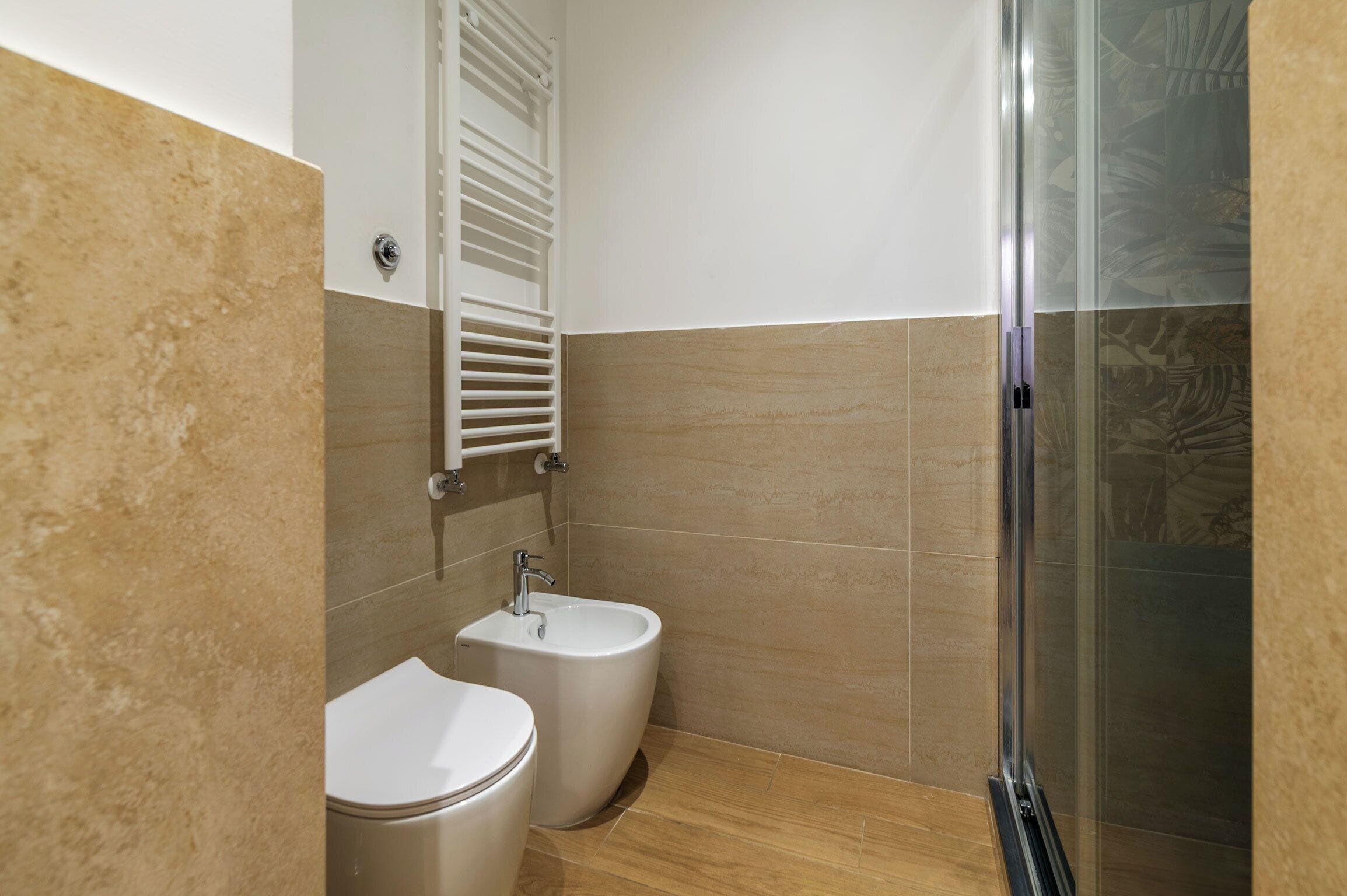 Un baño con dos inodoros, un bidé, una ducha con puerta de cristal y un perchero para toallas.