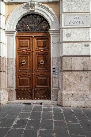 A large wooden double door with a metal gate above it, set in a stone building with a plaque reading "VIA CAVOUR". - JOIVY Cavour 238 (Rome)