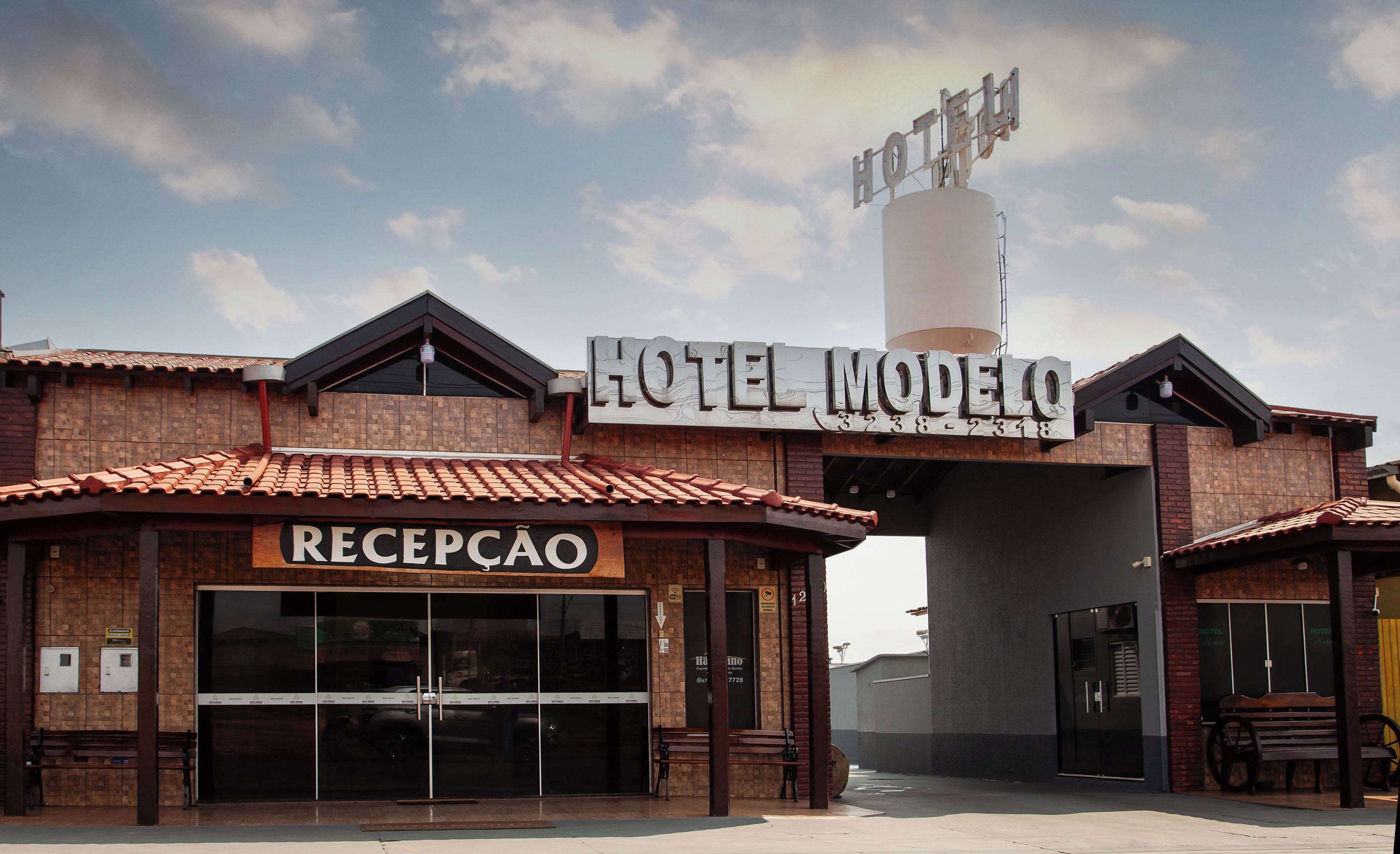 Entrada de un hotel con una recepción, un cartel grande que dice "HOTEL MODELO" y una estructura cilíndrica alta.