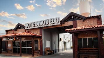 Hotel chamado "Hotel Modelo", com área de recepção, um reservatório de água grande e fachada rústica de tijolos.