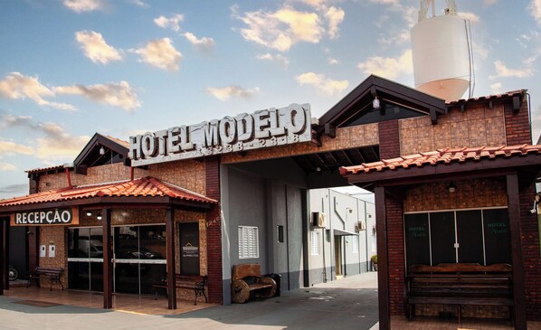 A hotel named "Hotel Modelo" with a reception area, a large water tank, and a rustic brick facade.