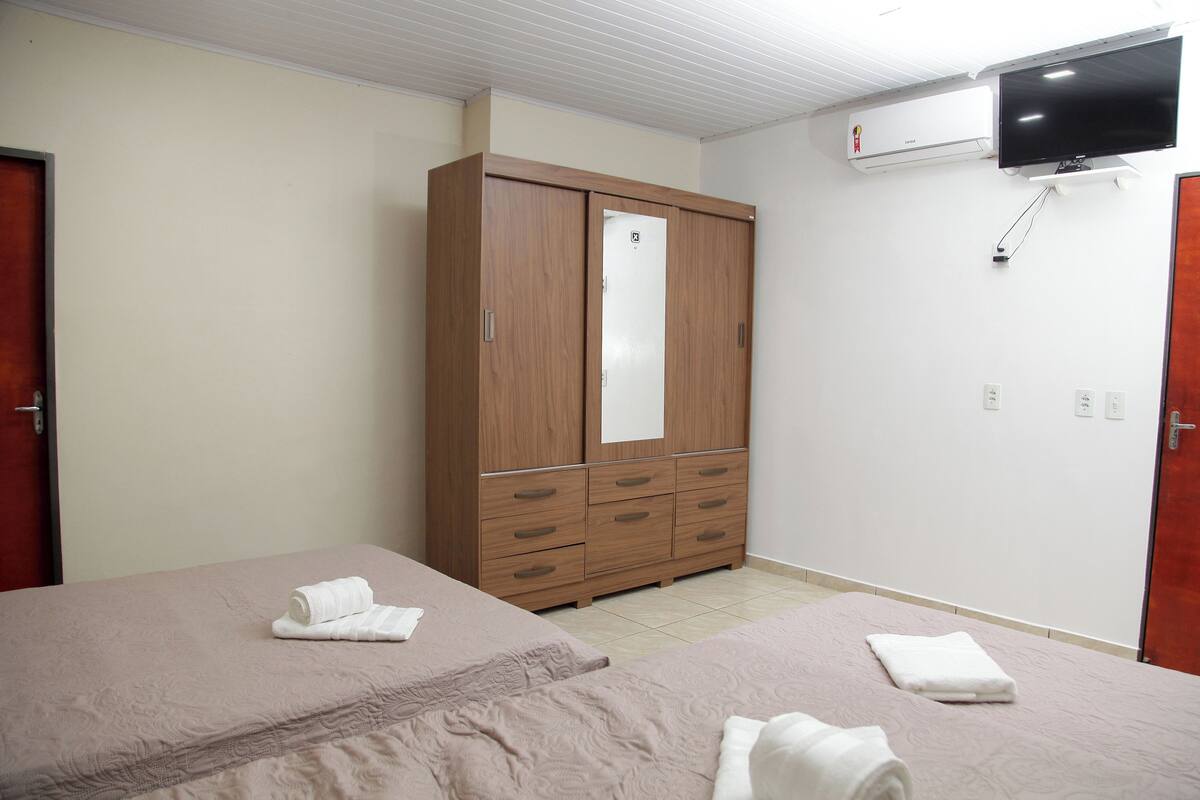 A hotel room with two beds, a wardrobe, a television, and an air conditioning unit.