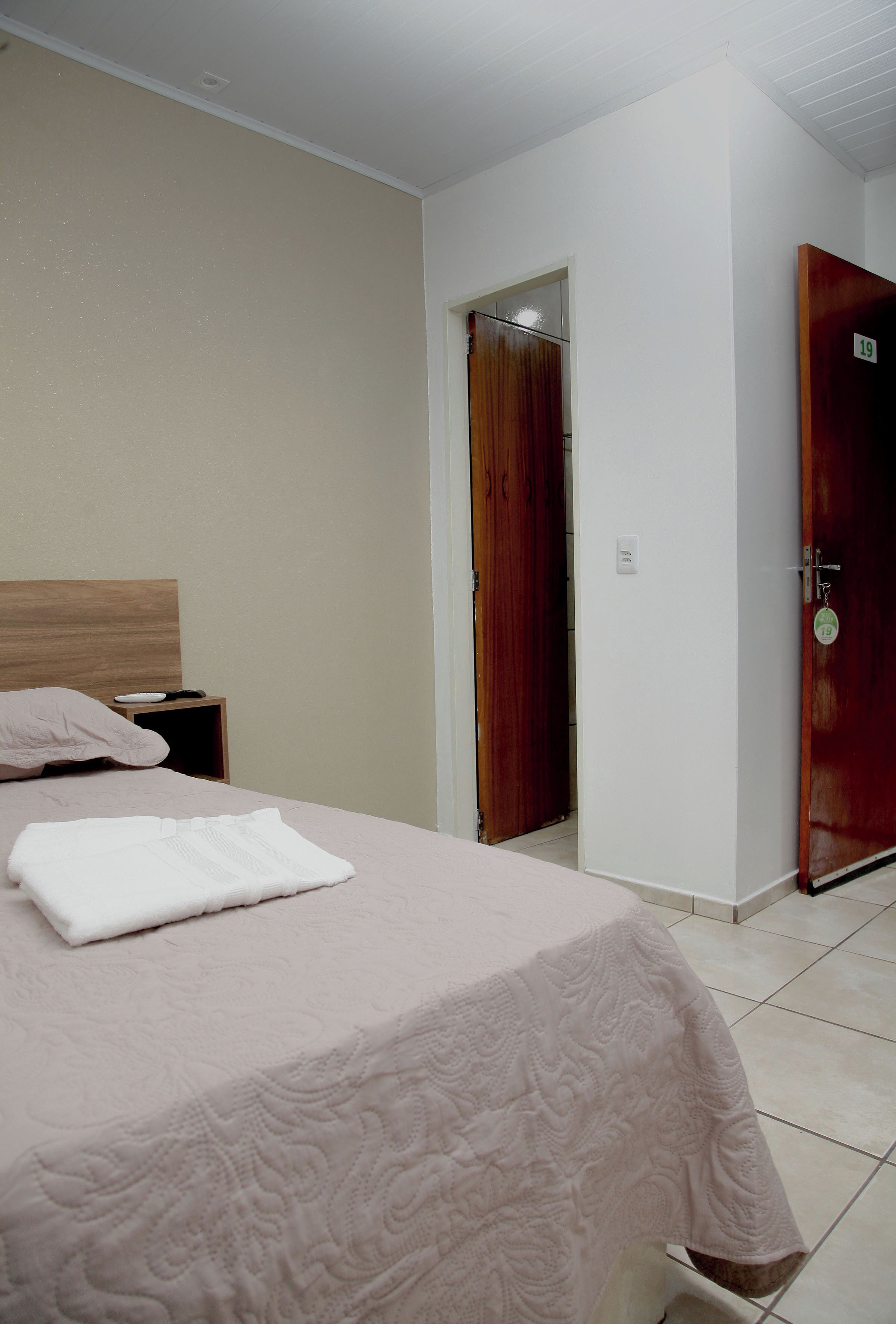 A bedroom with a bed, a nightstand, a wooden door, and a white wall.