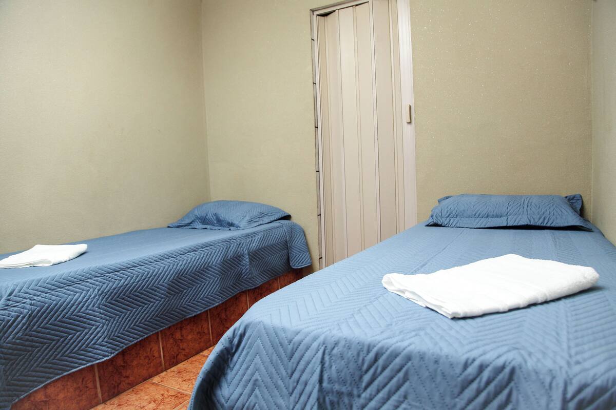 Two single beds with blue bedding, a wooden bench, and a closed door.