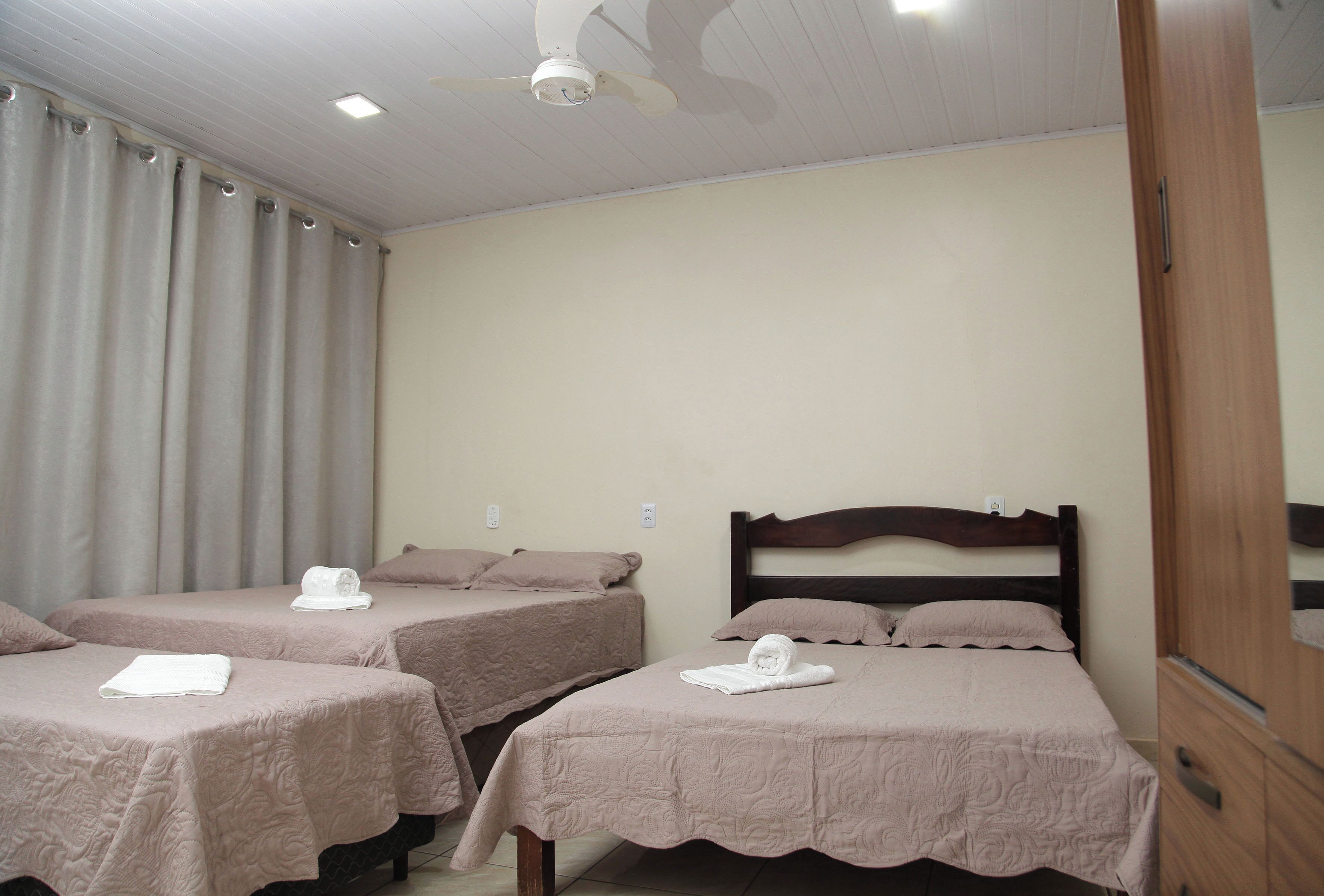 Une chambre d’hôtel avec trois lits simples, chacun agrémenté d’une serviette soigneusement pliée et d’un chapeau.