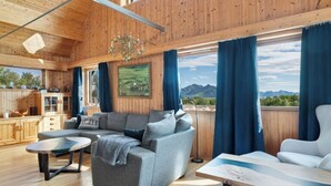 A cozy cabin interior with a wooden ceiling, a sofa, a dining table, and a view of mountains through large windows. - Bestefarhaugen - the Cozy House on the Hill,& Dome (Bø)