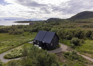 A large, dark-colored house with a sloped roof, surrounded by lush greenery and a dirt path leading to it. - Bestefarhaugen - the Cozy House on the Hill,& Dome (Bø)