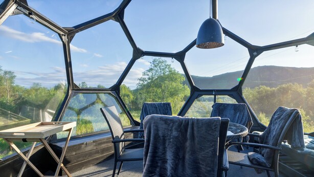 A hexagonal room with a table and chairs, large windows, and a view of the outdoors. - Bestefarhaugen - the Cozy House on the Hill,& Dome (Bø)
