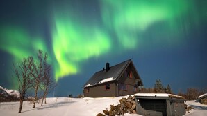 A house with a snow-covered roof and a garage, surrounded by a snowy landscape under a night sky with visible stars. - Bestefarhaugen - the Cozy House on the Hill,& Dome (Bø)