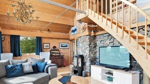 A cozy cabin interior with a stone wall, wooden staircase, and a television on a wooden cabinet. - Bestefarhaugen - the Cozy House on the Hill,& Dome (Bø)
