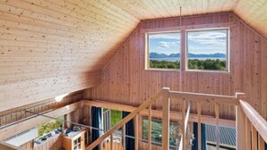 A wooden cabin with a loft bedroom, a balcony with outdoor seating, and a large window offering a view of mountains and greenery. - Bestefarhaugen - the Cozy House on the Hill,& Dome (Bø)