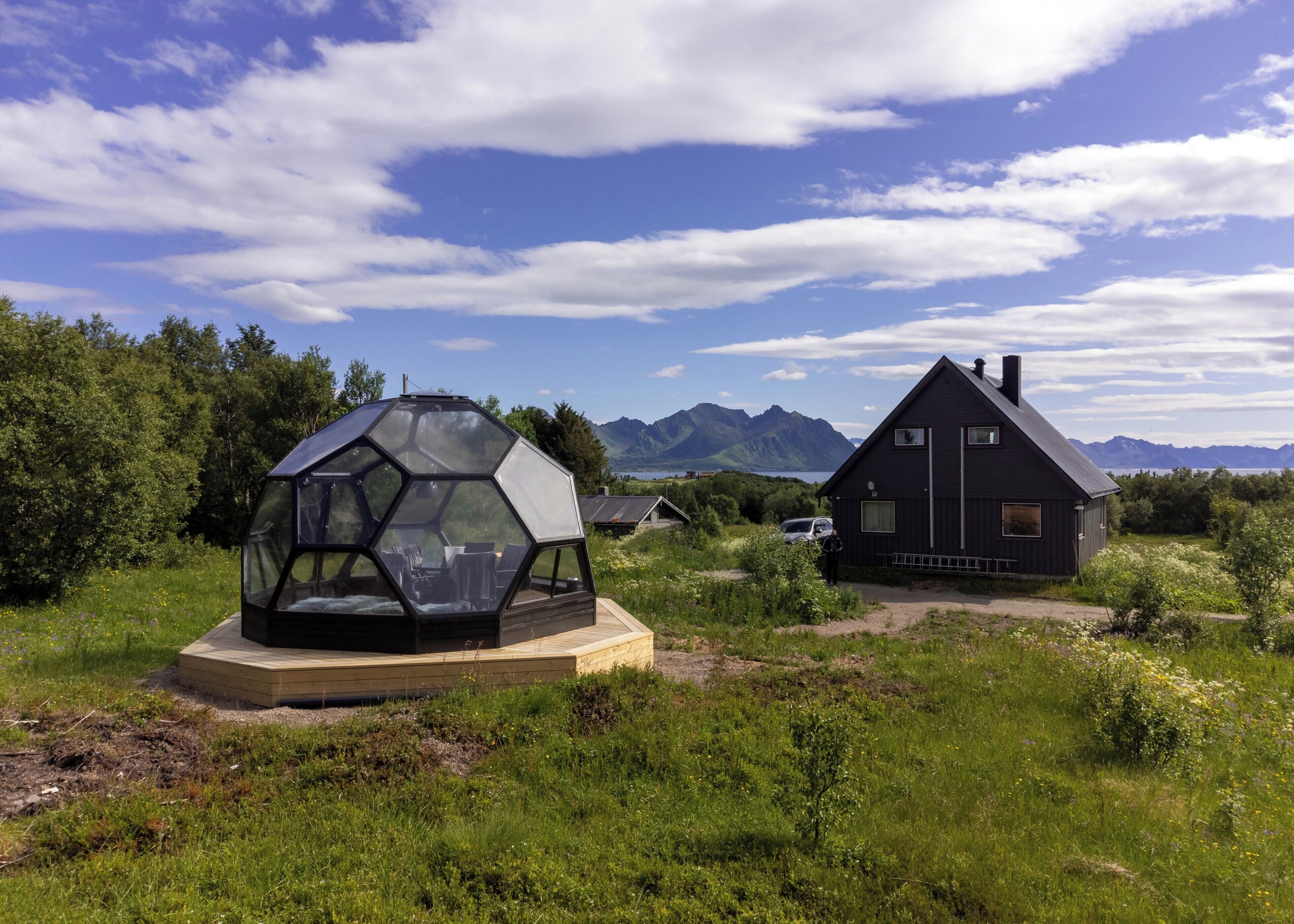 A geodesic dome structure and a dark wooden house with a mountain backdrop.