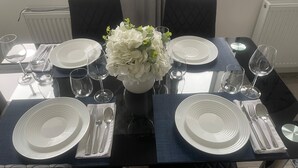 Een eettafel gedekt met witte borden, bestek en heldere wijnglazen, met een witte bloemstuk in het midden.