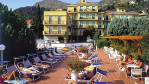 A rooftop pool area with sun loungers and umbrellas, surrounded by a yellow building with multiple balconies. - Apartment in Pietra Ligure With Garage (Pietra Ligure)