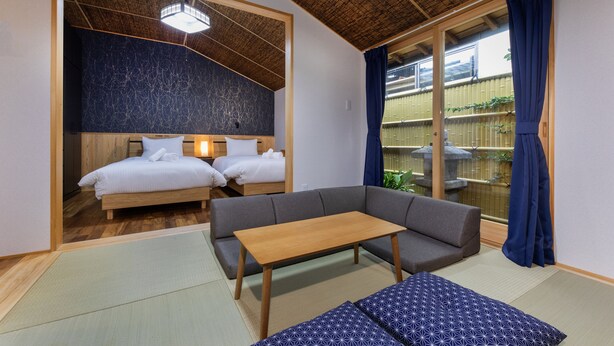 A room with a wooden ceiling, a sofa, a small table, and a bed with white bedding. - Gojo Furusato (Kyoto)