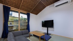 A living room with a sofa, a table, a TV, tatami mats, and a view of a garden through a sliding door. - Gojo Furusato (Kyoto)