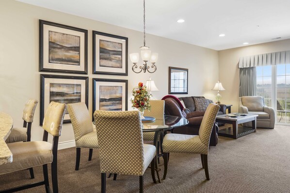 A hotel room with a dining area, a sofa, a coffee table, and framed artwork on the walls.
