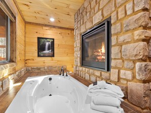 A bathroom with a large bathtub, a stone wall, and a fireplace. - NEW Luxury GBurg Cabin Private Pool-Theater-Games- Hot Tub (Gatlinburg)