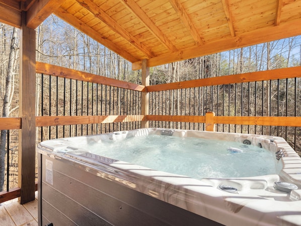 A wooden deck with a hot tub, surrounded by a forest.