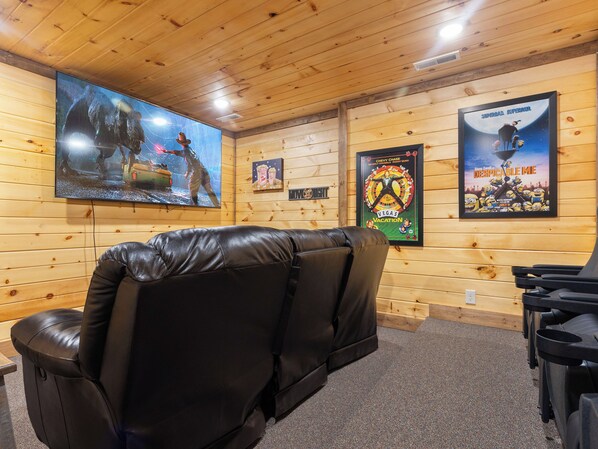 A cozy room with a large flat-screen TV mounted on the wall, a leather reclining chair, and a poster of 'Despicable Me' on the wall. - NEW Luxury GBurg Cabin Private Pool-Theater-Games- Hot Tub (Gatlinburg)