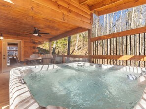A wooden cabin with a hot tub, wooden deck, and a view of trees.