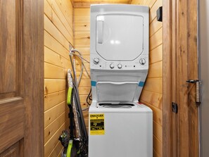 A compact, white washer and dryer unit with a control panel, placed in a wooden-paneled room.
