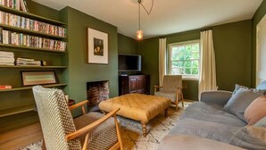 A cozy living room with a bookshelf, a fireplace, a television, and a comfortable sofa. - Host Stay Haclins Cottage (Fakenham)
