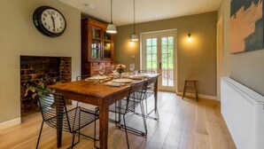 A dining area with a wooden table set for six, a fireplace, and a clock on the wall. - Host Stay Haclins Cottage (Fakenham)