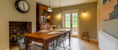 A dining area with a wooden table set for six, a fireplace, and a clock on the wall.