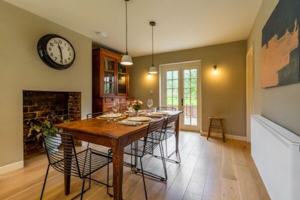 A dining area with a wooden table set for six, a fireplace, and a clock on the wall. - Host Stay Haclins Cottage (Fakenham)