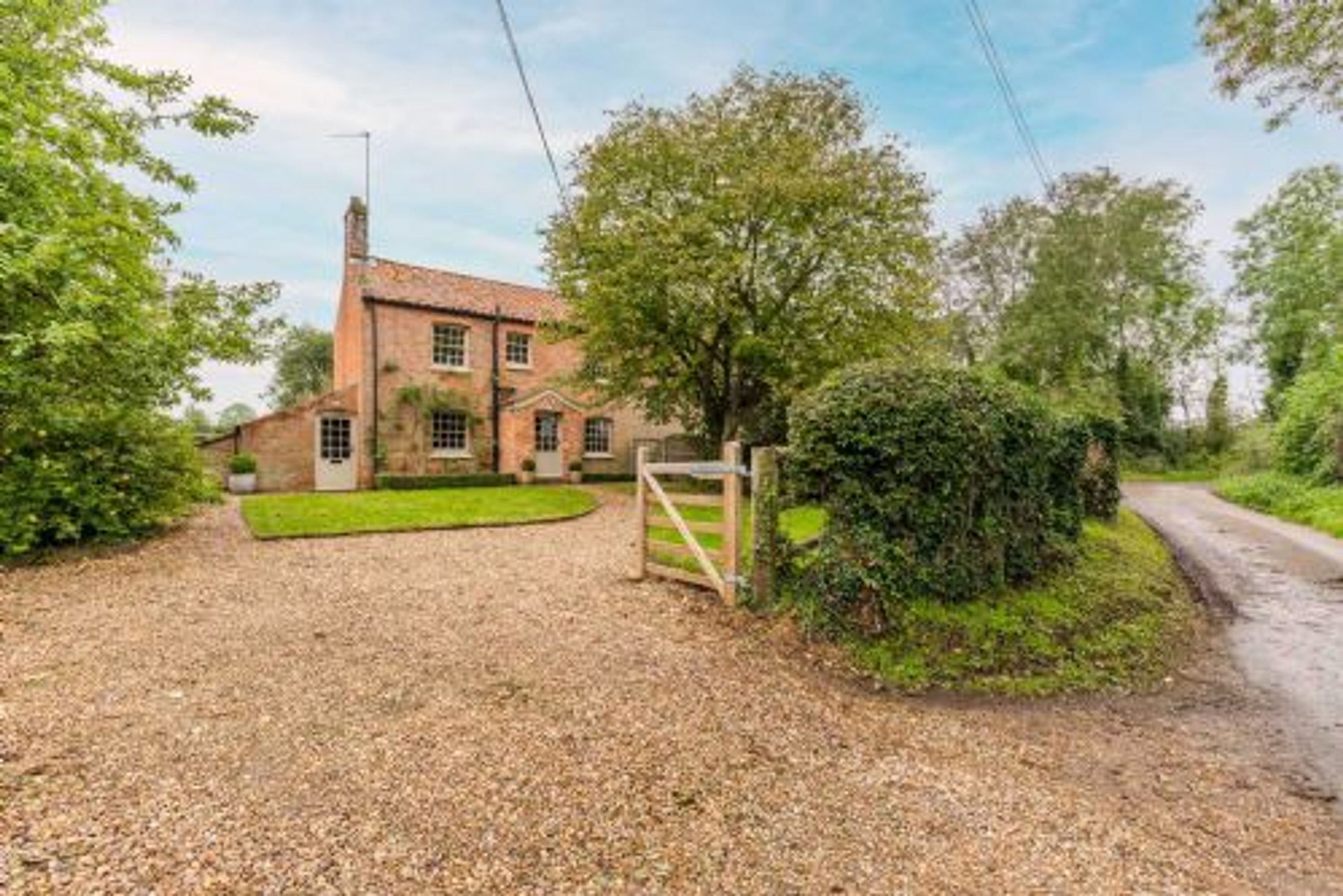 A traditional brick house with a gravel driveway and a wooden gate.