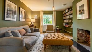 A cozy living room with a sofa, ottoman, and fireplace. - Host Stay Haclins Cottage (Fakenham)