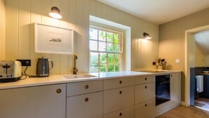 A kitchen with a large window, white cabinetry, and a toaster on the counter. - Host Stay Haclins Cottage (Fakenham)