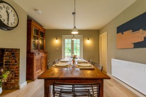 A dining room with a wooden table set for six, flanked by chairs, a brick wall, and a wooden cabinet. - Host Stay Haclins Cottage (Fakenham)