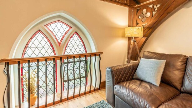 Una habitación con escalera de madera, sofá de cuero y un amplio ventanal de arco con vidrieras.