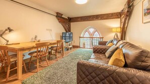 Una sala de estar acogedora con una mesa de comedor de madera, un sofá de cuero y un amplio ventanal con un arco decorativo.