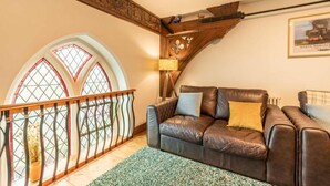Una sala de estar con un sofá de cuero marrón, techo de madera y una ventana con marco decorativo.