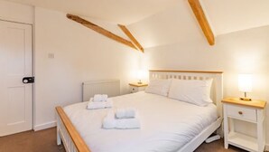 A bedroom with a wooden ceiling, a bed with white bedding, two bedside tables with lamps, and a radiator. - Host Stay 1 Ruscon Cottage (King's Lynn)