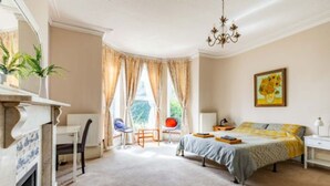 A bedroom with a bed, a chair, a desk, a fireplace, and a window with curtains.