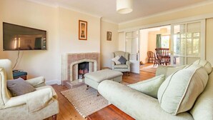 A living room with a fireplace, a sofa, a television, and a dining area with chairs. - Host Stay Welsford House (Norwich)