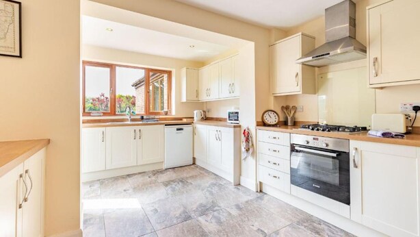 A modern kitchen with white cabinets, a built-in oven, and a window with a view of greenery. - Host Stay Welsford House (Norwich)